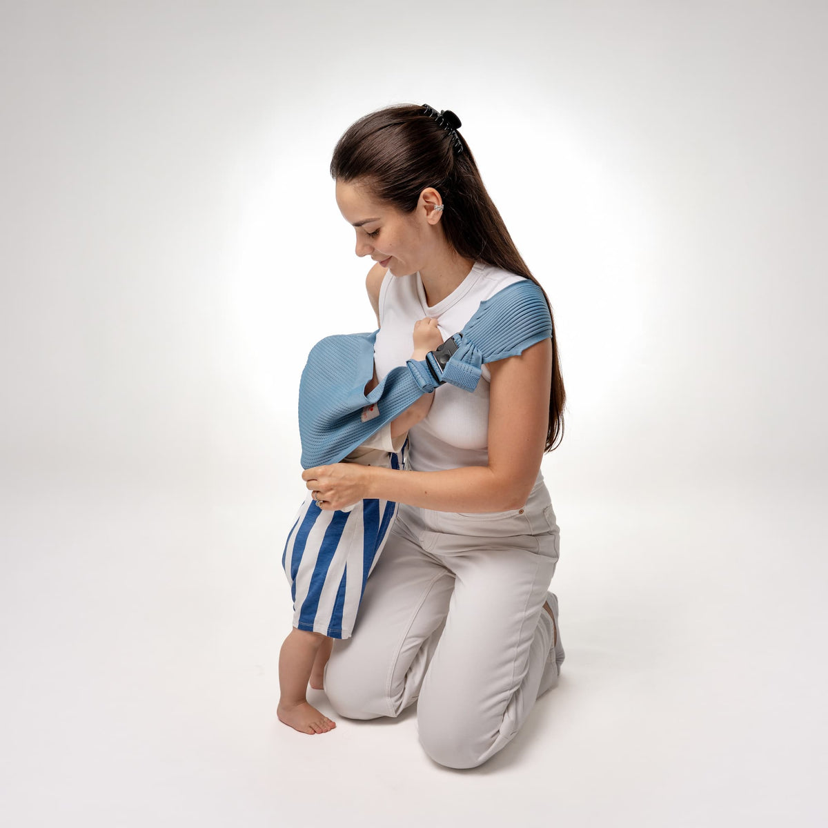 Coshen baby carrier user guide step 2: Bend knees to crouch, pass over baby's head, and wrap around body.