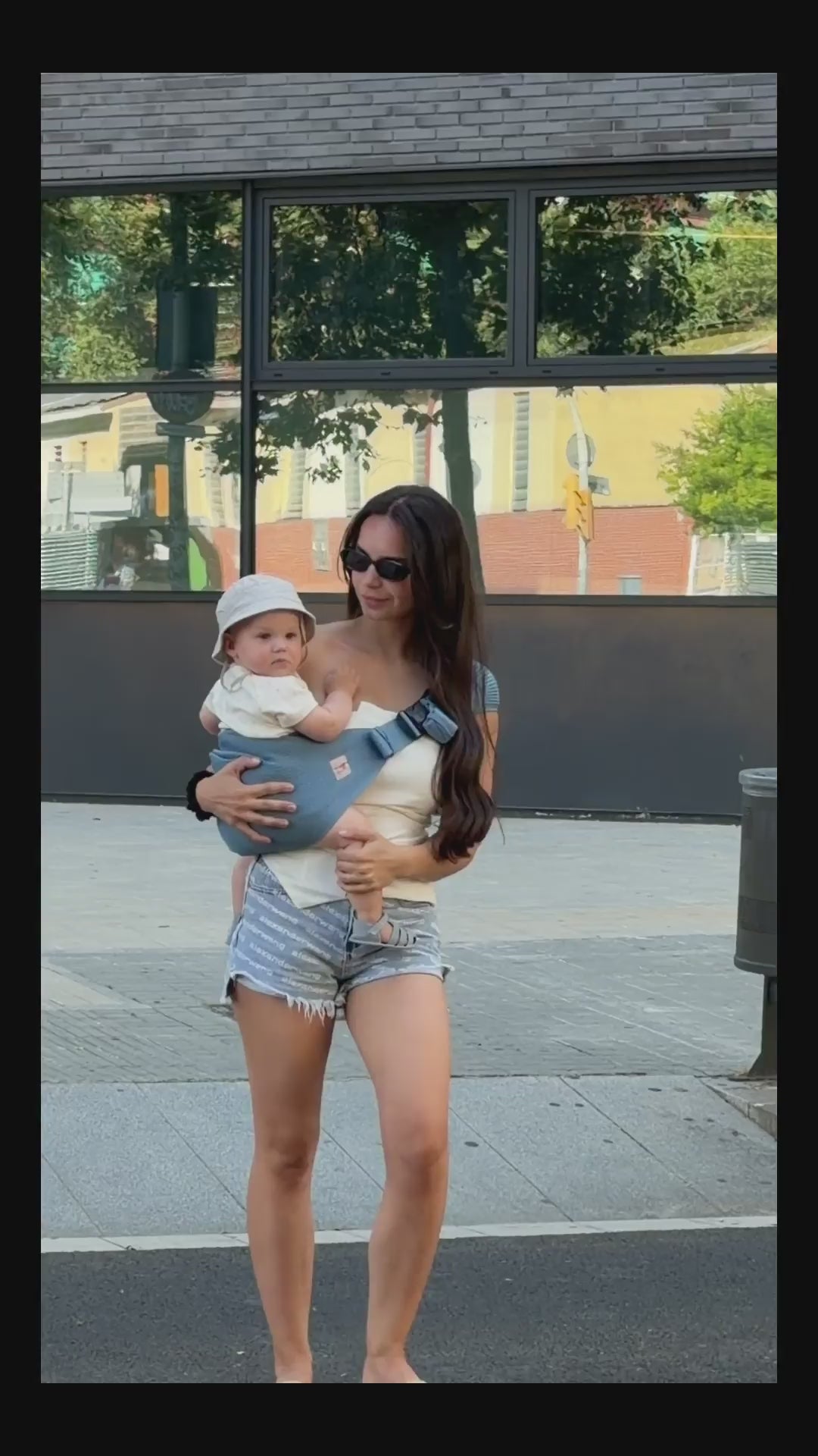Coshen Coral Blue Toddler Hip Carrier Lifestyle Video. Mother using a seamless 3D knit hip carrier for easy one-hand support during a city walk, showcasing the durable safety buckle and the healthy, ergonomic M-position for comfortable toddler carrying.